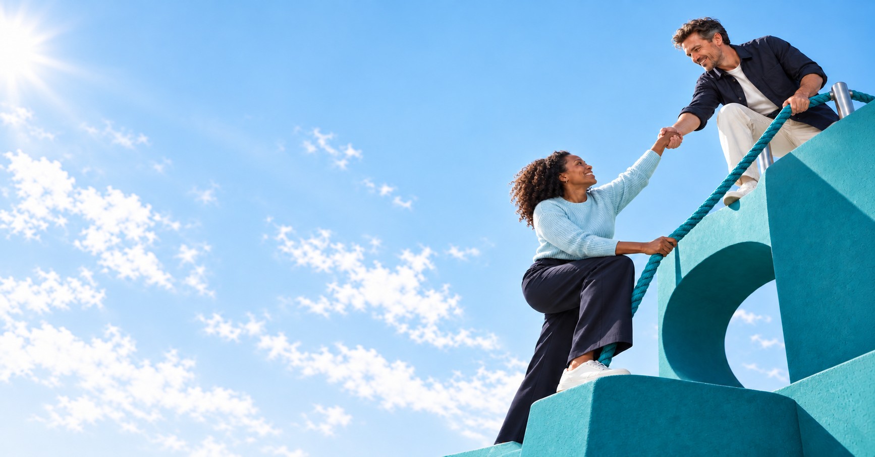 A man helping a woman climb teal steps using a teal rope beneath a bright sky.